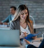 Young happy businesswoman reading reports while going through paperwork and working with a colleague in the office.