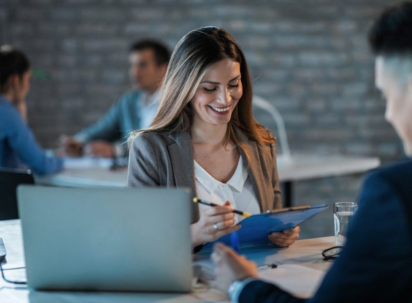 Young happy businesswoman reading reports while going through paperwork and working with a colleague in the office.