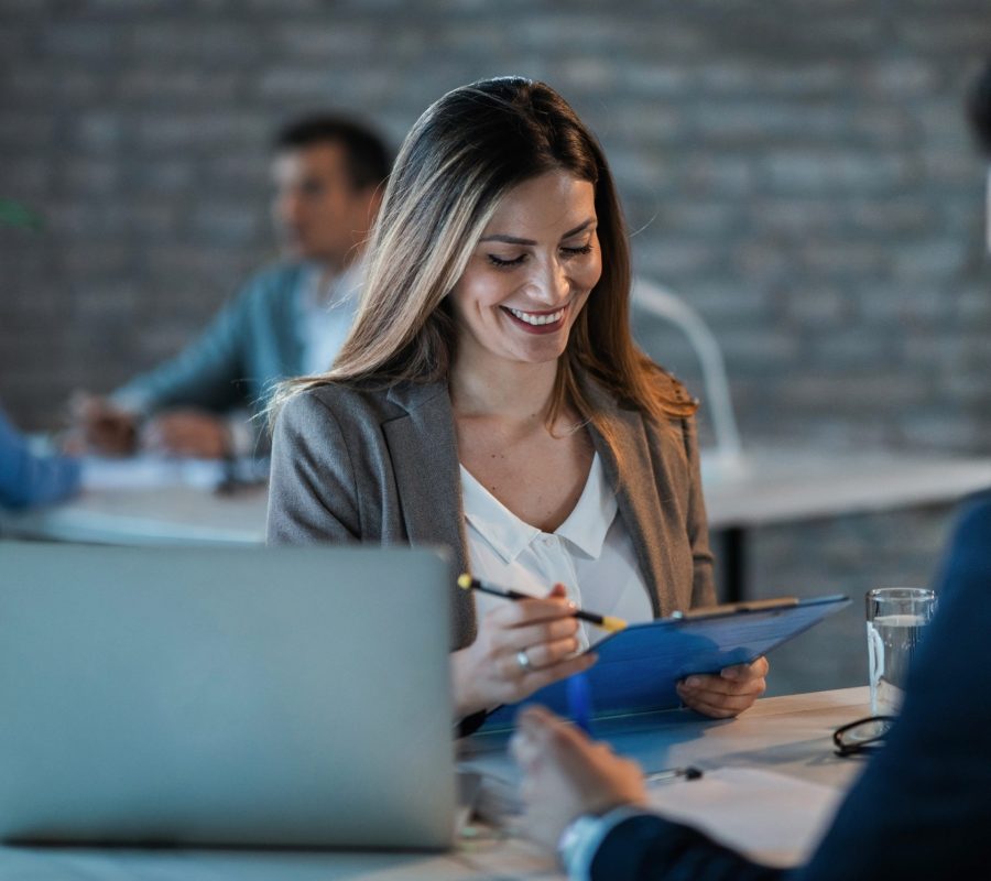 Young happy businesswoman reading reports while going through paperwork and working with a colleague in the office.
